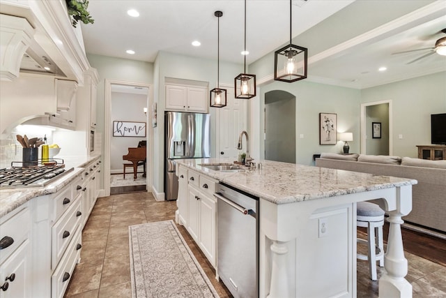 kitchen with arched walkways, a sink, custom range hood, light stone countertops, and appliances with stainless steel finishes