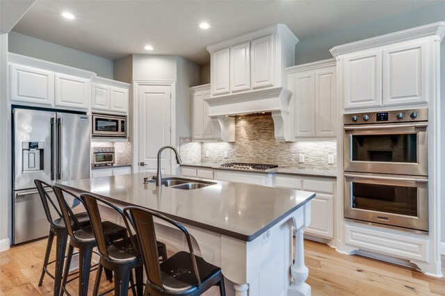 kitchen with light wood finished floors, stainless steel appliances, a sink, tasteful backsplash, and white cabinetry