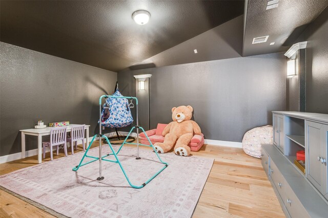 playroom featuring vaulted ceiling, wood finished floors, visible vents, and baseboards