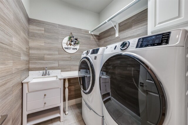 washroom featuring light tile patterned floors, a sink, tile walls, washing machine and clothes dryer, and cabinet space