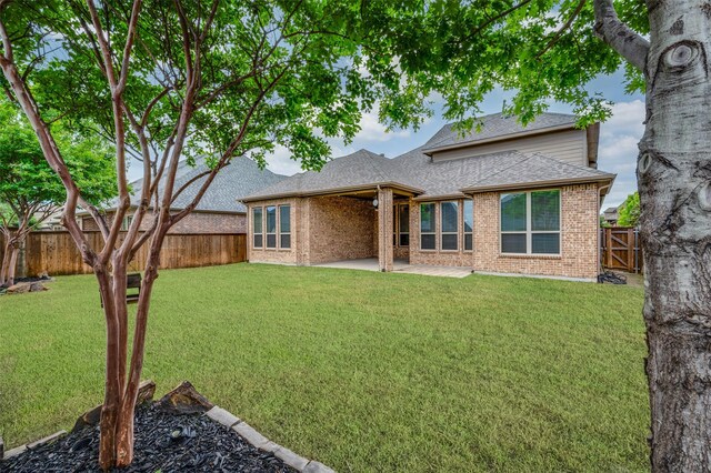 back of property featuring brick siding, a patio area, a fenced backyard, a yard, and roof with shingles