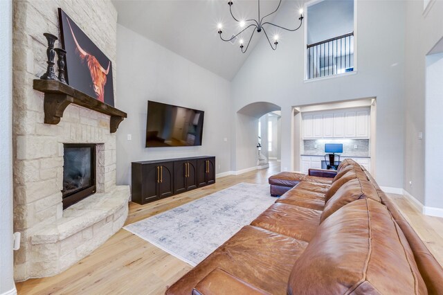 living room featuring arched walkways, light wood-type flooring, baseboards, a stone fireplace, and high vaulted ceiling