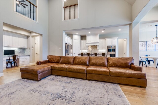 living room with recessed lighting, a chandelier, a towering ceiling, and light wood-type flooring