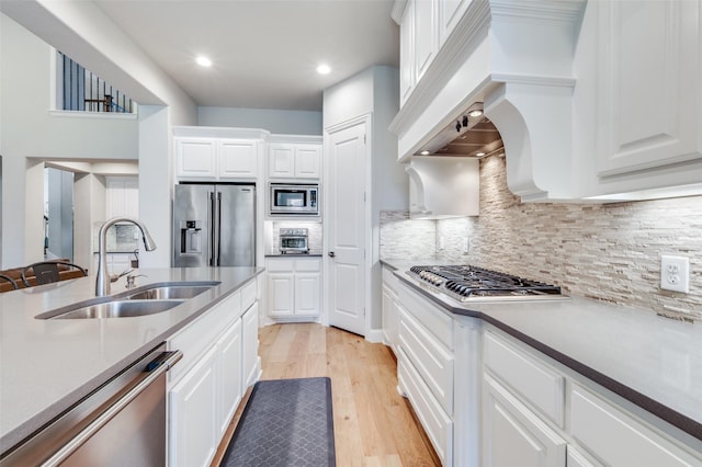 kitchen with stainless steel appliances, a sink, tasteful backsplash, light wood-type flooring, and white cabinetry