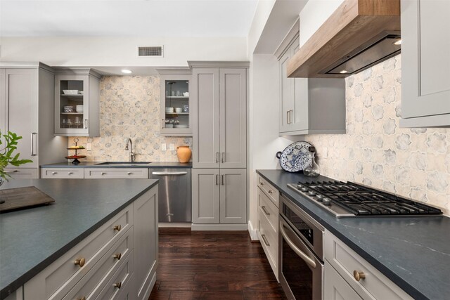 kitchen with dark countertops, visible vents, a sink, wall chimney exhaust hood, and appliances with stainless steel finishes