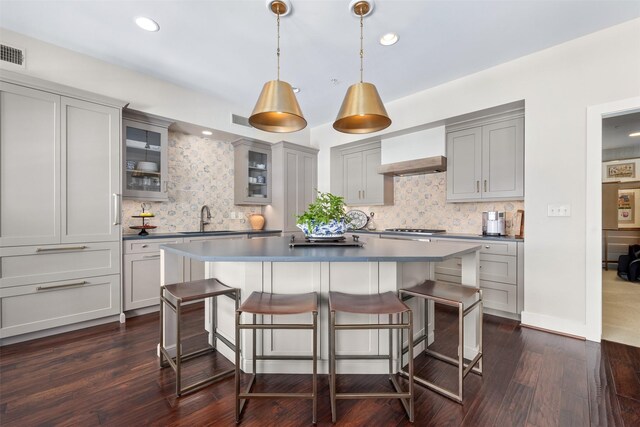 kitchen with a kitchen breakfast bar, gray cabinets, a sink, wall chimney exhaust hood, and decorative backsplash