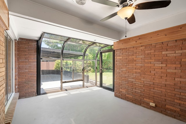 interior space with finished concrete floors, a wealth of natural light, ceiling fan, and brick wall