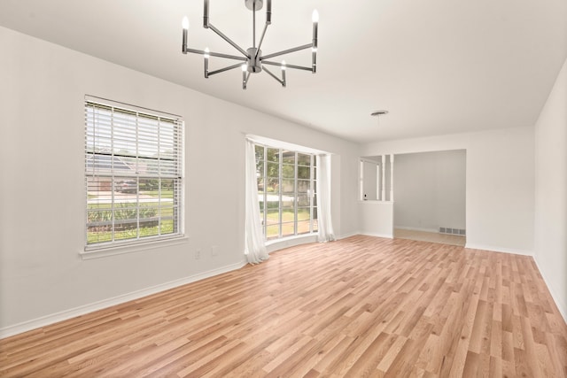 spare room featuring an inviting chandelier, baseboards, light wood-type flooring, and visible vents
