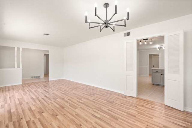 unfurnished room featuring light wood finished floors, an inviting chandelier, and visible vents