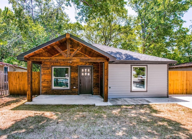 view of front of property featuring fence, a shingled roof, and a patio