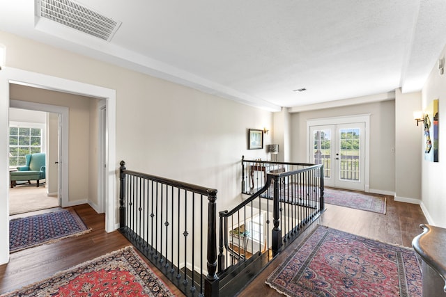 hallway with an upstairs landing, visible vents, wood finished floors, and baseboards