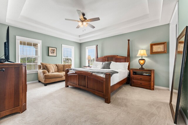 bedroom with a raised ceiling, baseboards, a ceiling fan, and light carpet
