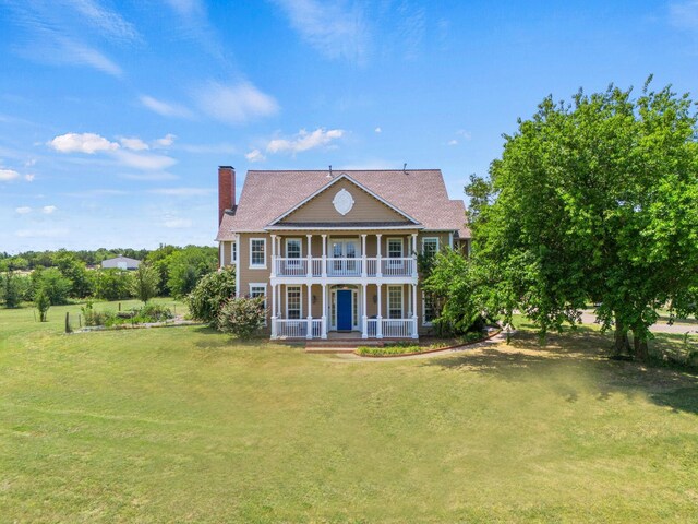 back of property with a chimney, a garden, covered porch, a balcony, and a lawn