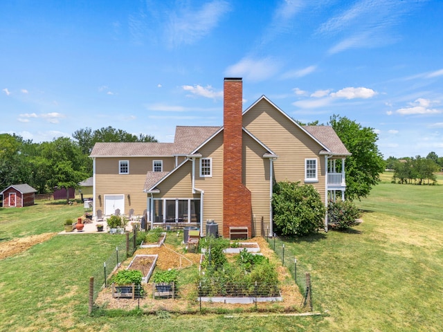 back of property featuring a storage unit, a chimney, an outbuilding, a lawn, and a vegetable garden