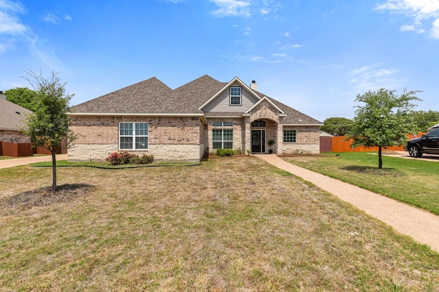 view of front of home with a chimney, fence, a front yard, brick siding, and roof with shingles