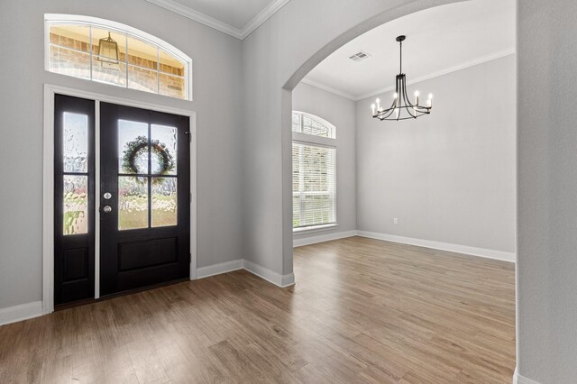 entryway with arched walkways, visible vents, a notable chandelier, wood finished floors, and crown molding