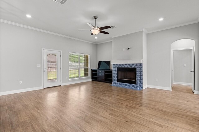 unfurnished living room with light wood finished floors, ornamental molding, arched walkways, a fireplace, and ceiling fan