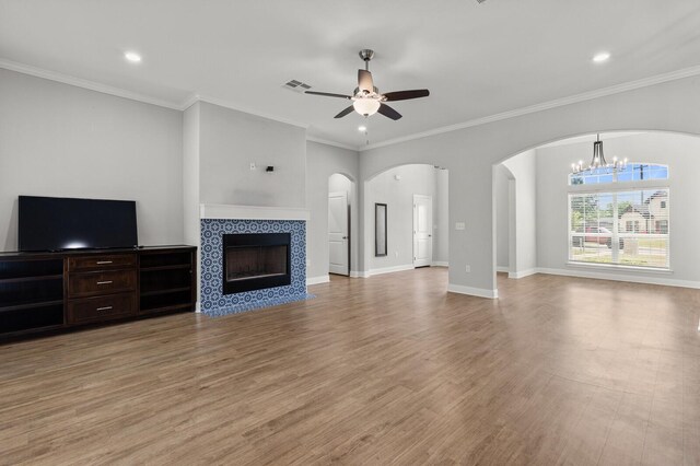 unfurnished living room with ceiling fan with notable chandelier, light wood-type flooring, arched walkways, a tile fireplace, and recessed lighting
