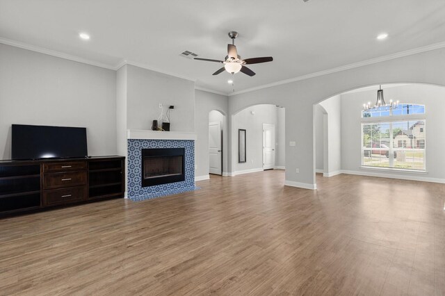unfurnished living room featuring recessed lighting, a tile fireplace, arched walkways, light wood-style floors, and ceiling fan with notable chandelier