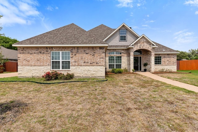 view of front of property with brick siding, fence, roof with shingles, and a front yard