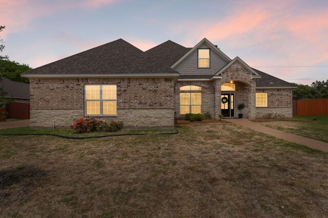 view of front of home featuring brick siding, a yard, roof with shingles, and fence