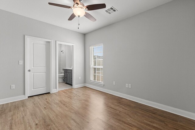 unfurnished bedroom featuring ensuite bath, wood finished floors, visible vents, and baseboards