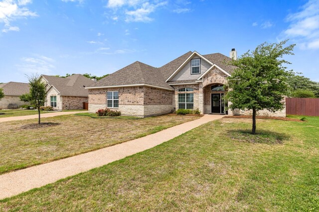 view of front of house with a chimney, fence, roof with shingles, brick siding, and a front yard