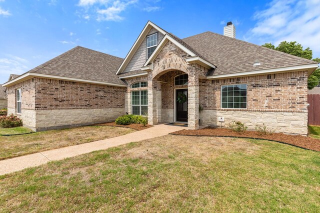 view of front of property featuring brick siding, a shingled roof, and a front yard