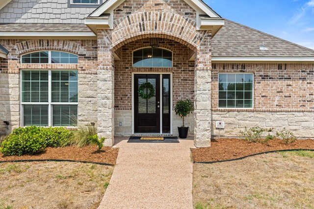 doorway to property with brick siding and roof with shingles