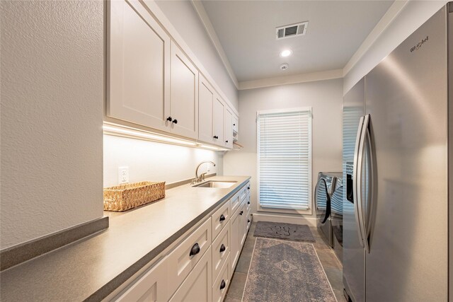 interior space featuring a sink, cabinet space, washing machine and dryer, ornamental molding, and visible vents