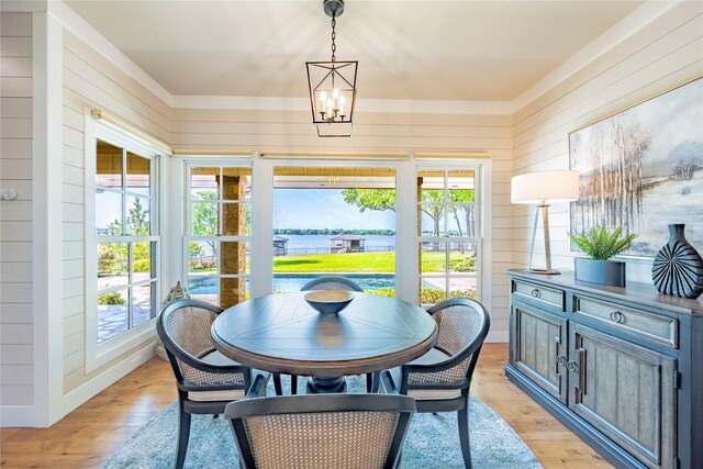 dining room with a notable chandelier, light wood-style floors, wooden walls, and a water view
