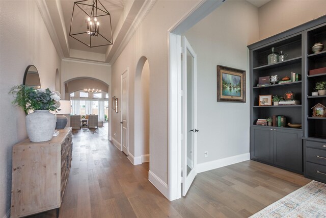 corridor with arched walkways, wood finished floors, baseboards, an inviting chandelier, and ornamental molding