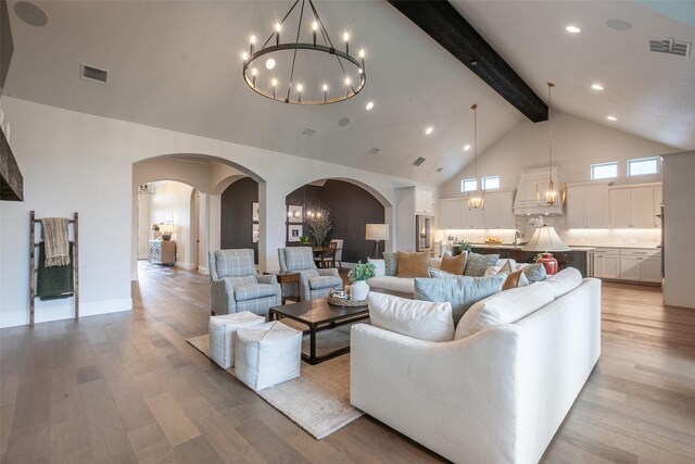 living area with a notable chandelier, beam ceiling, arched walkways, light wood-style flooring, and visible vents