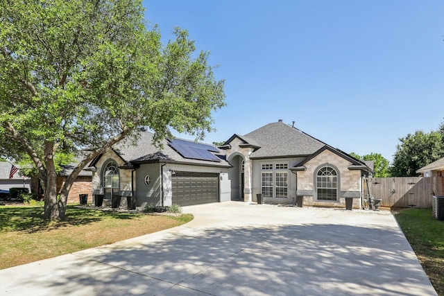 french country home featuring fence, roof mounted solar panels, cooling unit, concrete driveway, and an attached garage