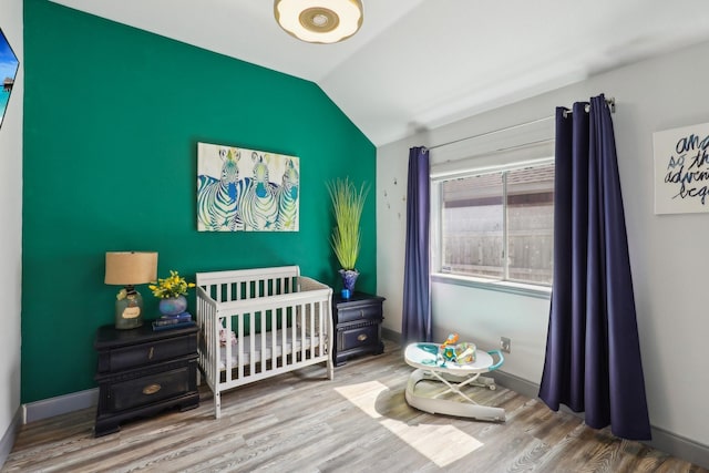 bedroom featuring a nursery area, vaulted ceiling, wood finished floors, and baseboards