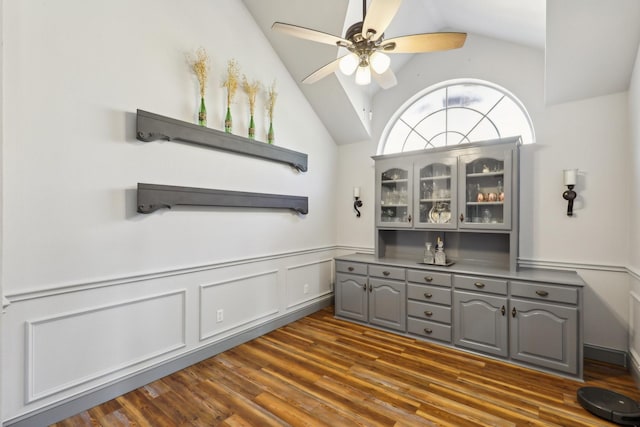 bar featuring wainscoting, lofted ceiling, a ceiling fan, and dark wood-type flooring
