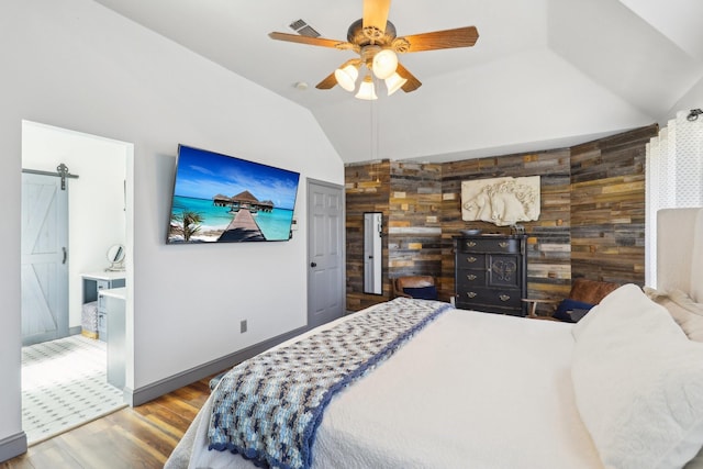 bedroom with a barn door, vaulted ceiling, visible vents, wood finished floors, and wooden walls