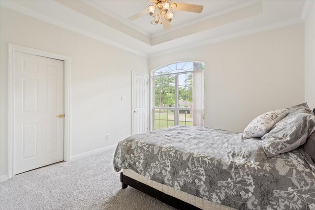 carpeted bedroom with a tray ceiling, crown molding, baseboards, and a ceiling fan