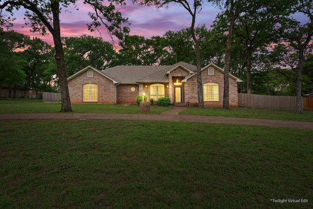 single story home featuring brick siding, fence, and a front yard