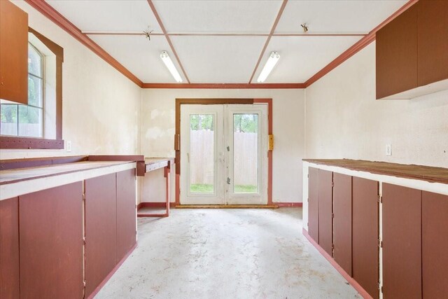 kitchen featuring unfinished concrete floors, baseboards, ornamental molding, and french doors