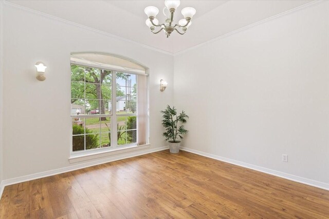 unfurnished room with an inviting chandelier, ornamental molding, wood finished floors, and baseboards