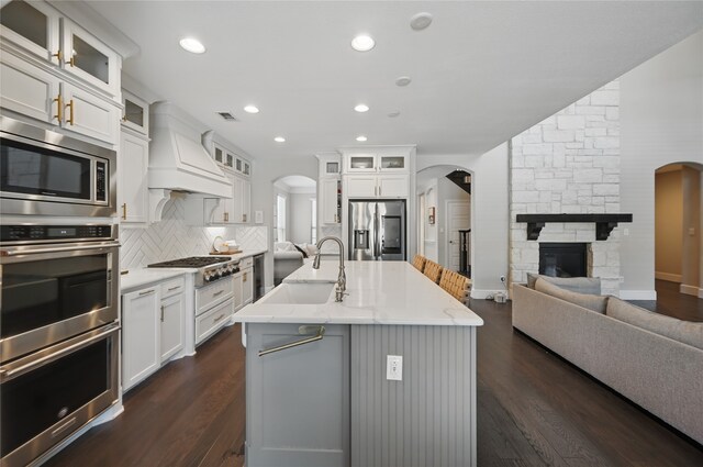 kitchen featuring a sink, arched walkways, a stone fireplace, stainless steel appliances, and visible vents