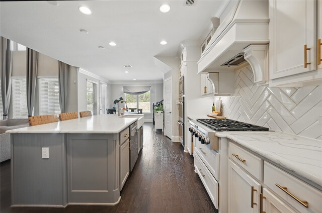 kitchen featuring light stone countertops, a center island with sink, stainless steel appliances, tasteful backsplash, and dark wood-style floors