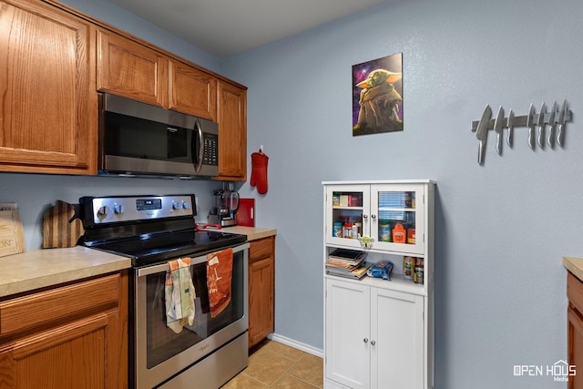 kitchen featuring light tile patterned floors, brown cabinets, stainless steel appliances, and light countertops