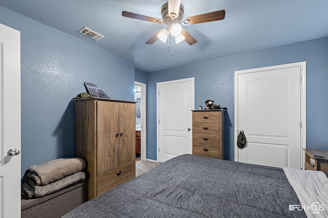 bedroom with a textured wall, visible vents, and ceiling fan