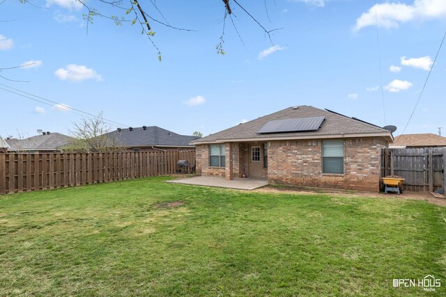rear view of property featuring roof mounted solar panels, a fenced backyard, a patio, a lawn, and brick siding