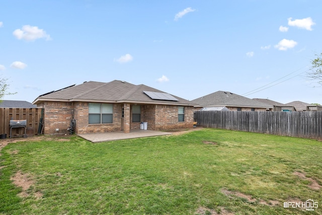 back of house with a lawn, a fenced backyard, roof mounted solar panels, a patio, and brick siding