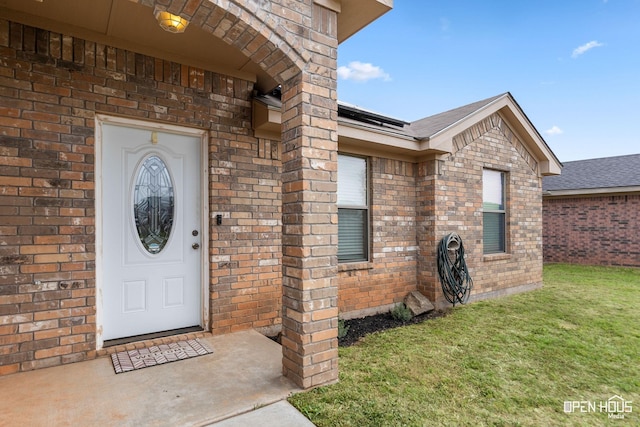 view of exterior entry featuring brick siding, a yard, and roof with shingles