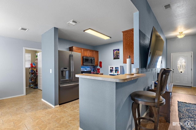 kitchen featuring brown cabinets, visible vents, a kitchen breakfast bar, and stainless steel appliances