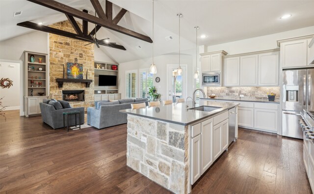 kitchen featuring an island with sink, stainless steel appliances, a sink, decorative light fixtures, and lofted ceiling with beams